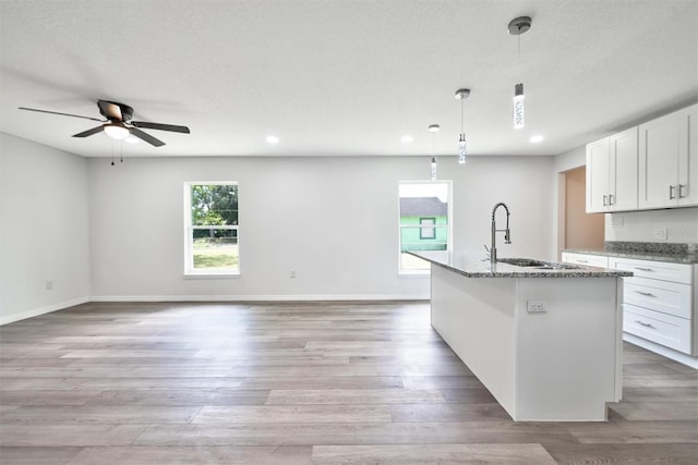 kitchen featuring hanging light fixtures, white cabinetry, ceiling fan, light hardwood / wood-style flooring, and dark stone counters