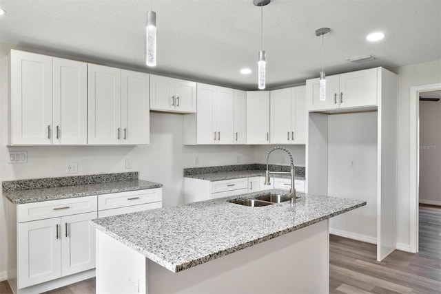 kitchen featuring pendant lighting, an island with sink, sink, light hardwood / wood-style flooring, and white cabinetry