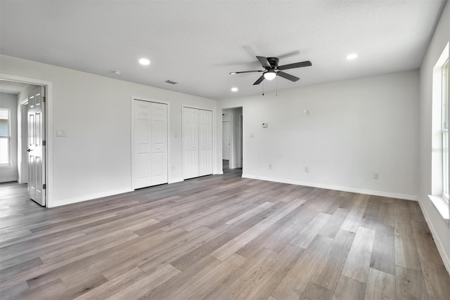 unfurnished bedroom with light wood-type flooring, multiple closets, ceiling fan, and a textured ceiling