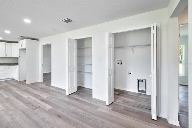 interior space with light wood-type flooring, a textured ceiling, and multiple closets