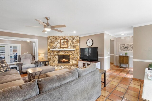 tiled living room with crown molding, ceiling fan, a stone fireplace, and french doors