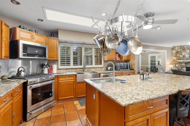 kitchen featuring appliances with stainless steel finishes, light stone counters, sink, ceiling fan, and decorative backsplash