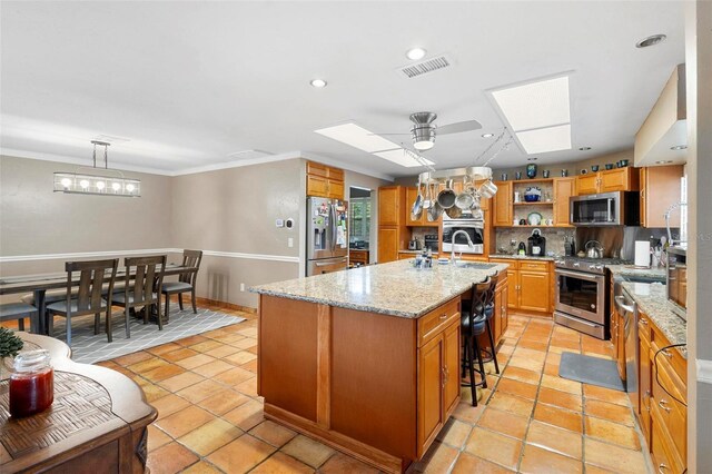 kitchen featuring light stone countertops, appliances with stainless steel finishes, an island with sink, a skylight, and ceiling fan