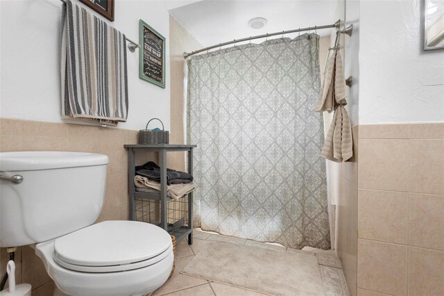 bathroom with tile walls, toilet, curtained shower, and tile patterned floors