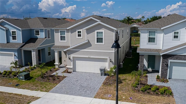 view of front facade with decorative driveway, cooling unit, a residential view, roof with shingles, and an attached garage