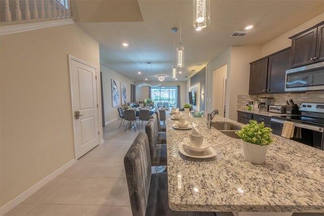 kitchen with backsplash, light stone countertops, appliances with stainless steel finishes, decorative light fixtures, and sink