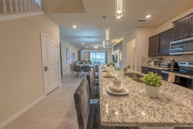 kitchen featuring light tile patterned floors, a sink, decorative backsplash, dark brown cabinets, and appliances with stainless steel finishes