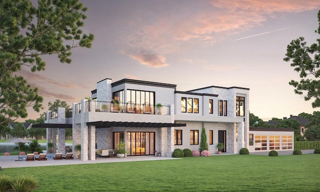 back house at dusk with a balcony, a patio area, and a yard