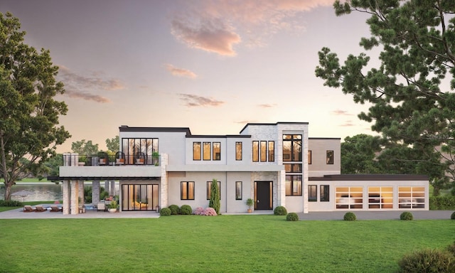 back house at dusk with a patio, a balcony, and a lawn