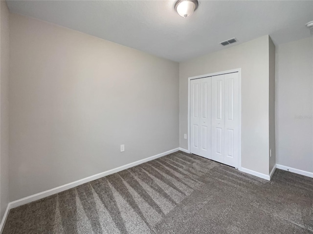 unfurnished bedroom with dark carpet and a closet