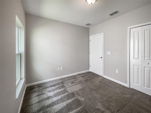 unfurnished bedroom with dark colored carpet and a closet