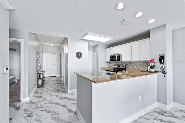 kitchen featuring appliances with stainless steel finishes, light stone countertops, kitchen peninsula, decorative backsplash, and white cabinets