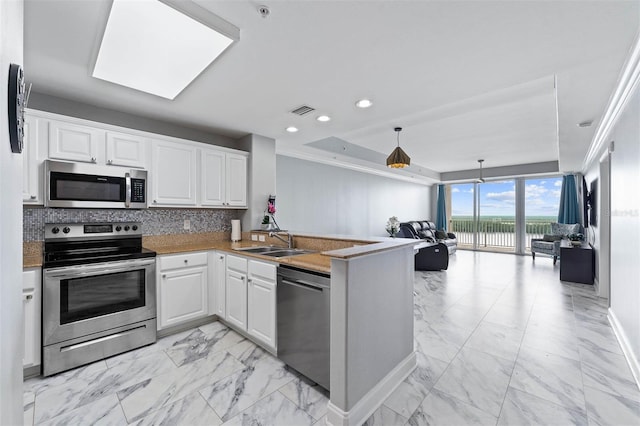 kitchen featuring stainless steel appliances, sink, white cabinetry, a raised ceiling, and kitchen peninsula