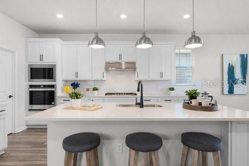 kitchen featuring built in microwave, sink, pendant lighting, a center island with sink, and oven