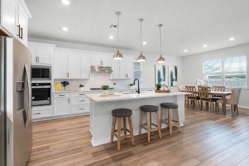 kitchen with pendant lighting, white cabinetry, stainless steel appliances, and an island with sink