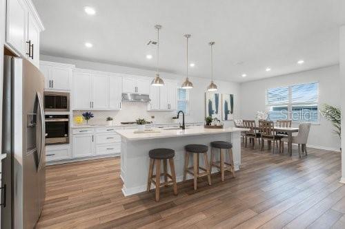 kitchen with pendant lighting, stainless steel fridge, white cabinets, and a kitchen island with sink