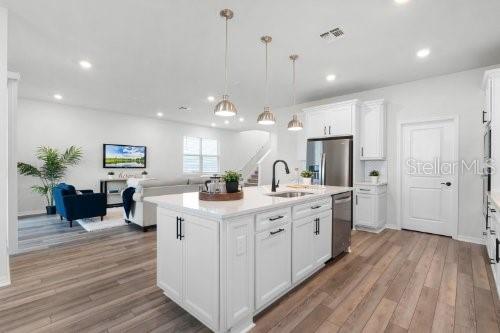 kitchen featuring a kitchen island with sink, hanging light fixtures, sink, appliances with stainless steel finishes, and white cabinetry