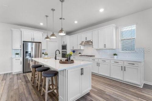 kitchen featuring white cabinets, decorative light fixtures, a center island with sink, and stainless steel appliances