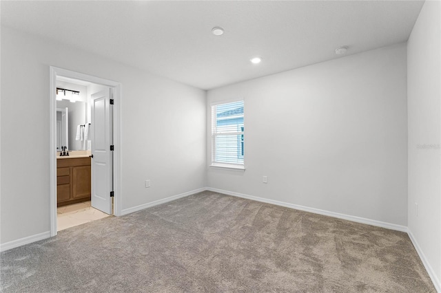 unfurnished bedroom featuring light colored carpet, ensuite bath, and sink