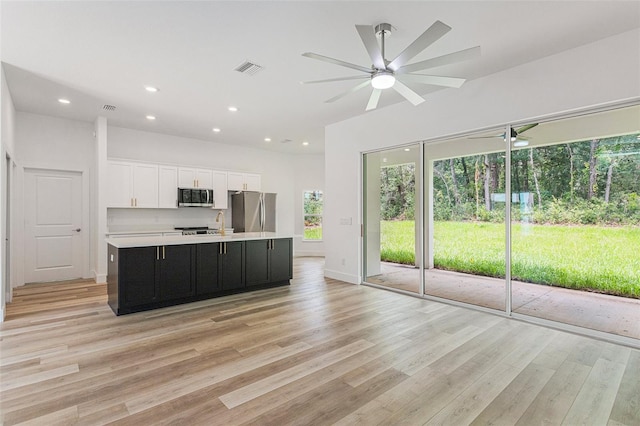 kitchen featuring ceiling fan, plenty of natural light, an island with sink, appliances with stainless steel finishes, and light hardwood / wood-style flooring