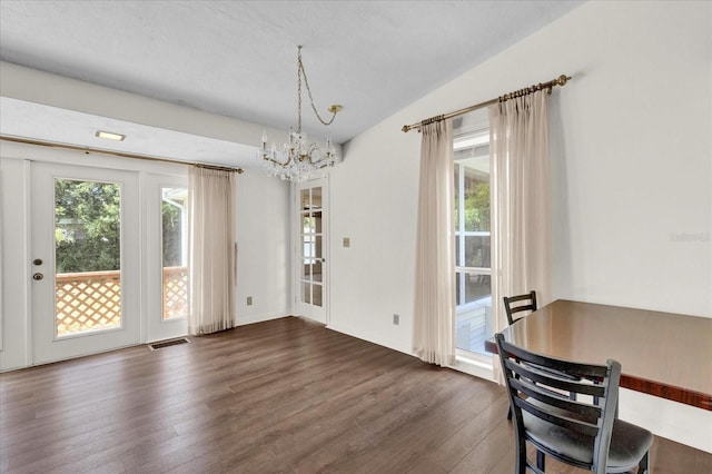 dining area with dark hardwood / wood-style floors, lofted ceiling, and an inviting chandelier