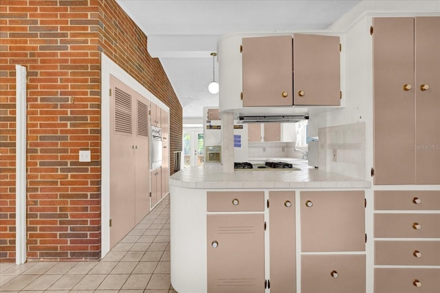 kitchen featuring kitchen peninsula, brick wall, stainless steel gas cooktop, light tile patterned floors, and oven