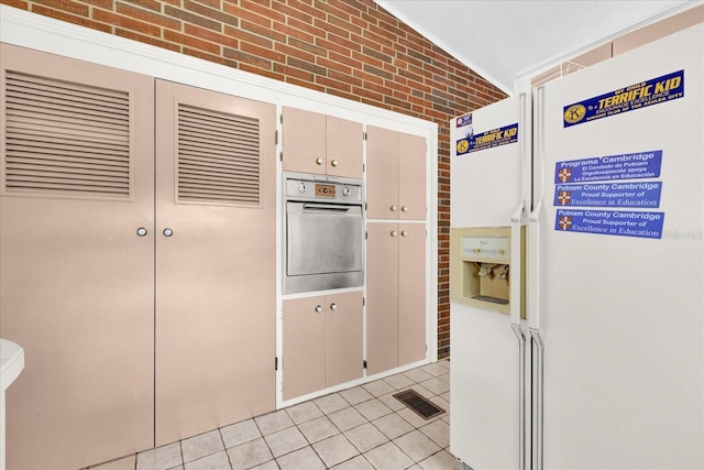 kitchen with brick wall, stainless steel oven, white refrigerator with ice dispenser, light tile patterned floors, and lofted ceiling