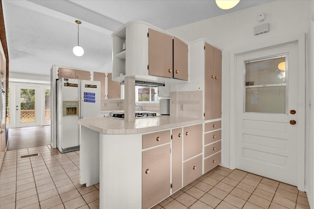 kitchen with decorative light fixtures, white refrigerator with ice dispenser, kitchen peninsula, and light tile patterned floors