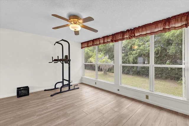 exercise area featuring ceiling fan, light wood-type flooring, and a textured ceiling