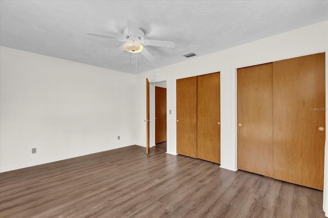 unfurnished bedroom with hardwood / wood-style flooring, ceiling fan, and two closets