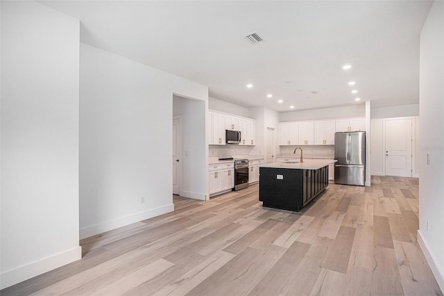 kitchen featuring appliances with stainless steel finishes, sink, light hardwood / wood-style floors, an island with sink, and white cabinetry