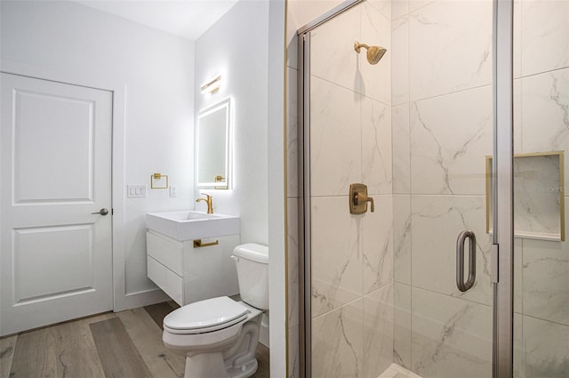 bathroom featuring wood-type flooring, a shower with door, toilet, and vanity