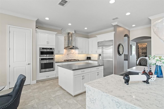 kitchen with crown molding, wall chimney exhaust hood, appliances with stainless steel finishes, tasteful backsplash, and white cabinetry