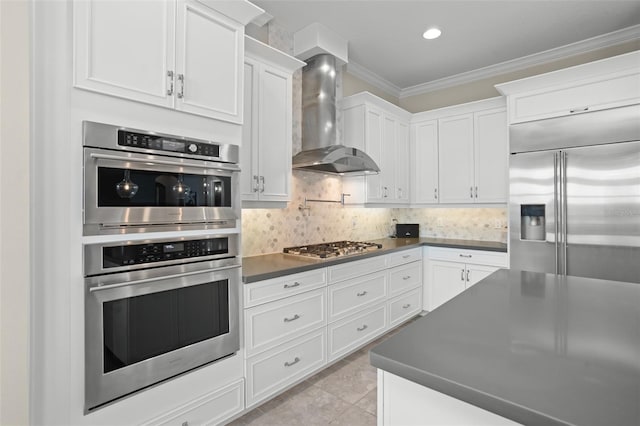 kitchen featuring white cabinets, wall chimney range hood, ornamental molding, tasteful backsplash, and stainless steel appliances