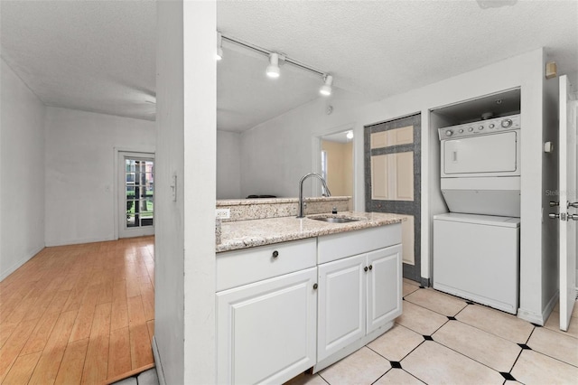 kitchen with sink, white cabinetry, stacked washer / dryer, and a textured ceiling