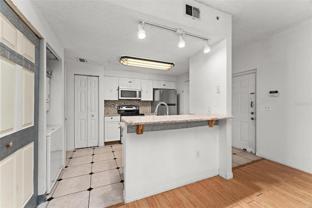 kitchen featuring appliances with stainless steel finishes, a textured ceiling, white cabinetry, a breakfast bar area, and independent washer and dryer