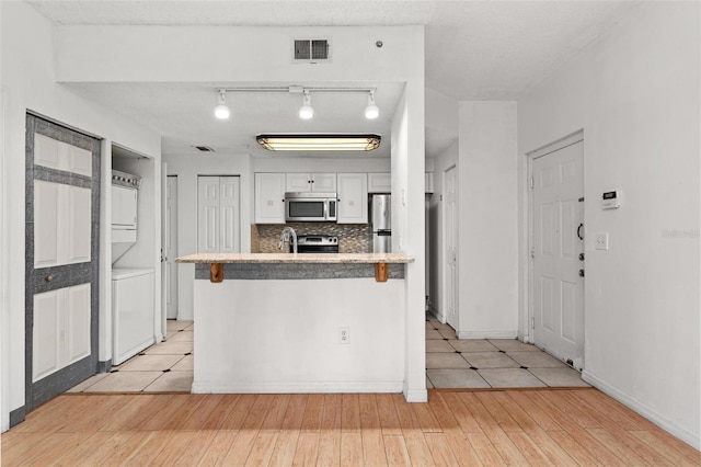 kitchen featuring a kitchen breakfast bar, appliances with stainless steel finishes, tasteful backsplash, white cabinetry, and stacked washer and clothes dryer