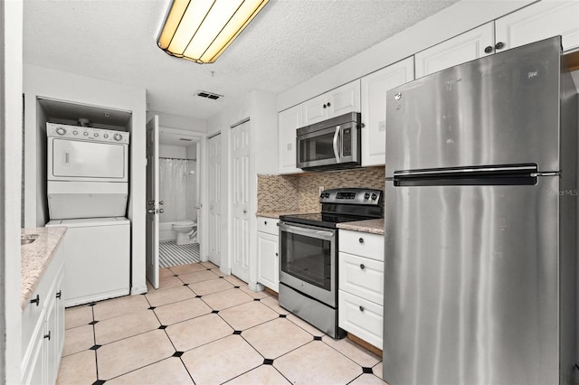 kitchen with light stone counters, white cabinets, stacked washer / drying machine, and stainless steel appliances