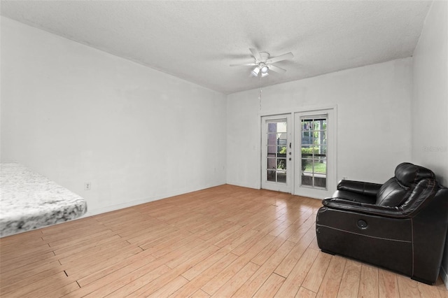 sitting room with light wood-type flooring, ceiling fan, and a textured ceiling