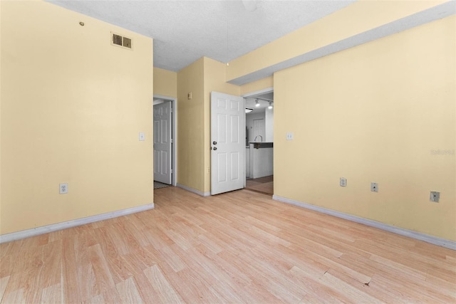 unfurnished room with light wood-type flooring and a textured ceiling