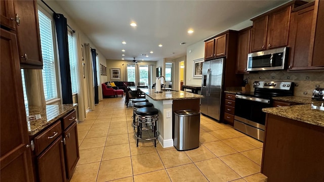 kitchen featuring sink, appliances with stainless steel finishes, a kitchen breakfast bar, light stone countertops, and a kitchen island with sink