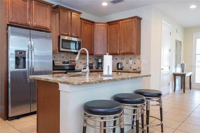 kitchen with light stone counters, backsplash, stainless steel appliances, and a breakfast bar