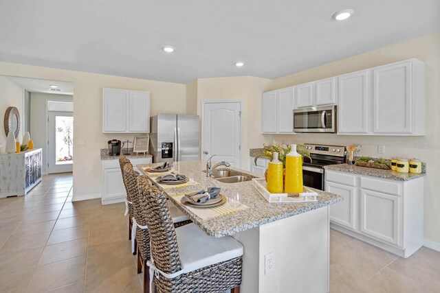 kitchen featuring a kitchen island with sink, white cabinets, sink, light tile patterned floors, and appliances with stainless steel finishes