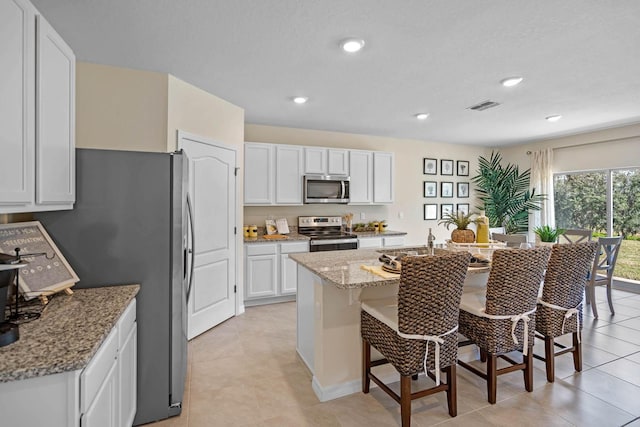 kitchen with a kitchen breakfast bar, light stone counters, stainless steel appliances, white cabinetry, and an island with sink