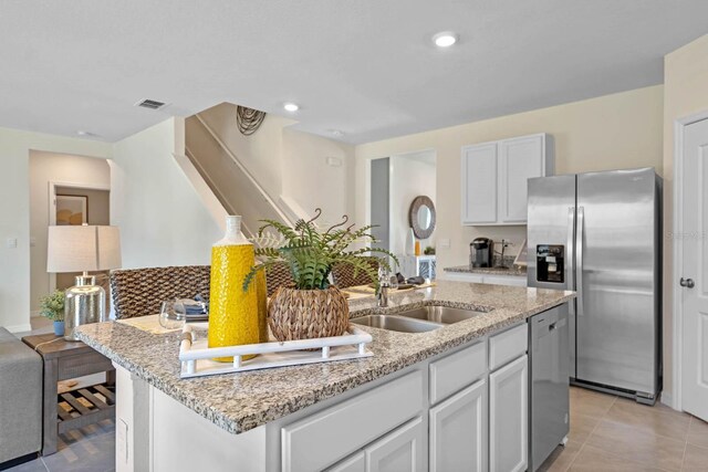 kitchen featuring light stone countertops, stainless steel appliances, a kitchen island with sink, sink, and white cabinetry