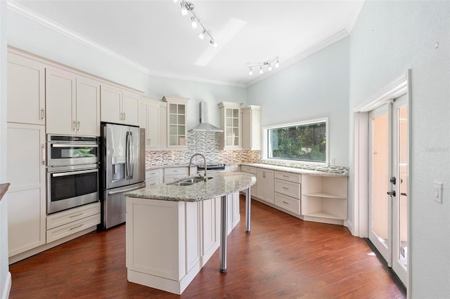 kitchen featuring light stone countertops, appliances with stainless steel finishes, wall chimney exhaust hood, a breakfast bar, and a center island with sink