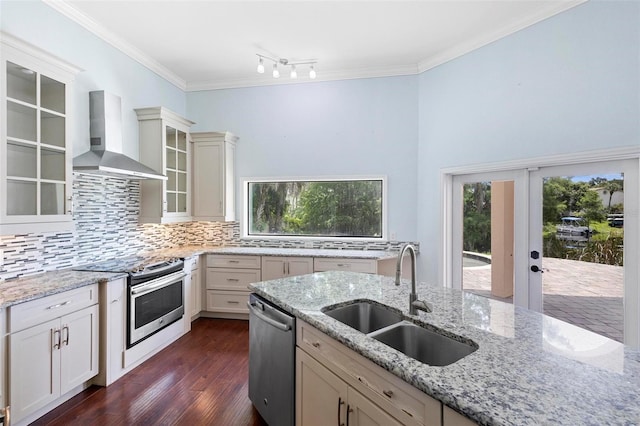 kitchen with appliances with stainless steel finishes, wall chimney exhaust hood, sink, backsplash, and light stone counters