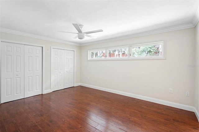 unfurnished bedroom featuring ceiling fan, dark wood-type flooring, crown molding, and multiple closets