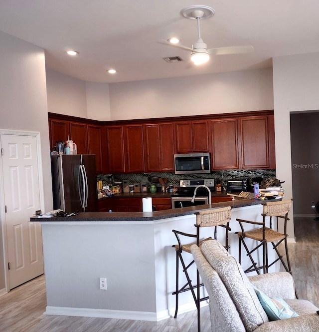 kitchen with appliances with stainless steel finishes, light wood-type flooring, ceiling fan, and backsplash