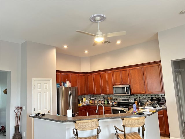 kitchen featuring a kitchen bar, ceiling fan, appliances with stainless steel finishes, and tasteful backsplash